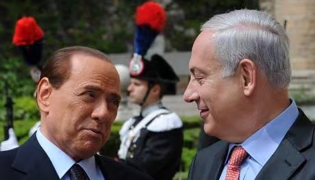 Silvio Berlusconi e Benjamin Netanyahu che si sorridono, con un carabiniere in alta uniforme sullo sfondo
